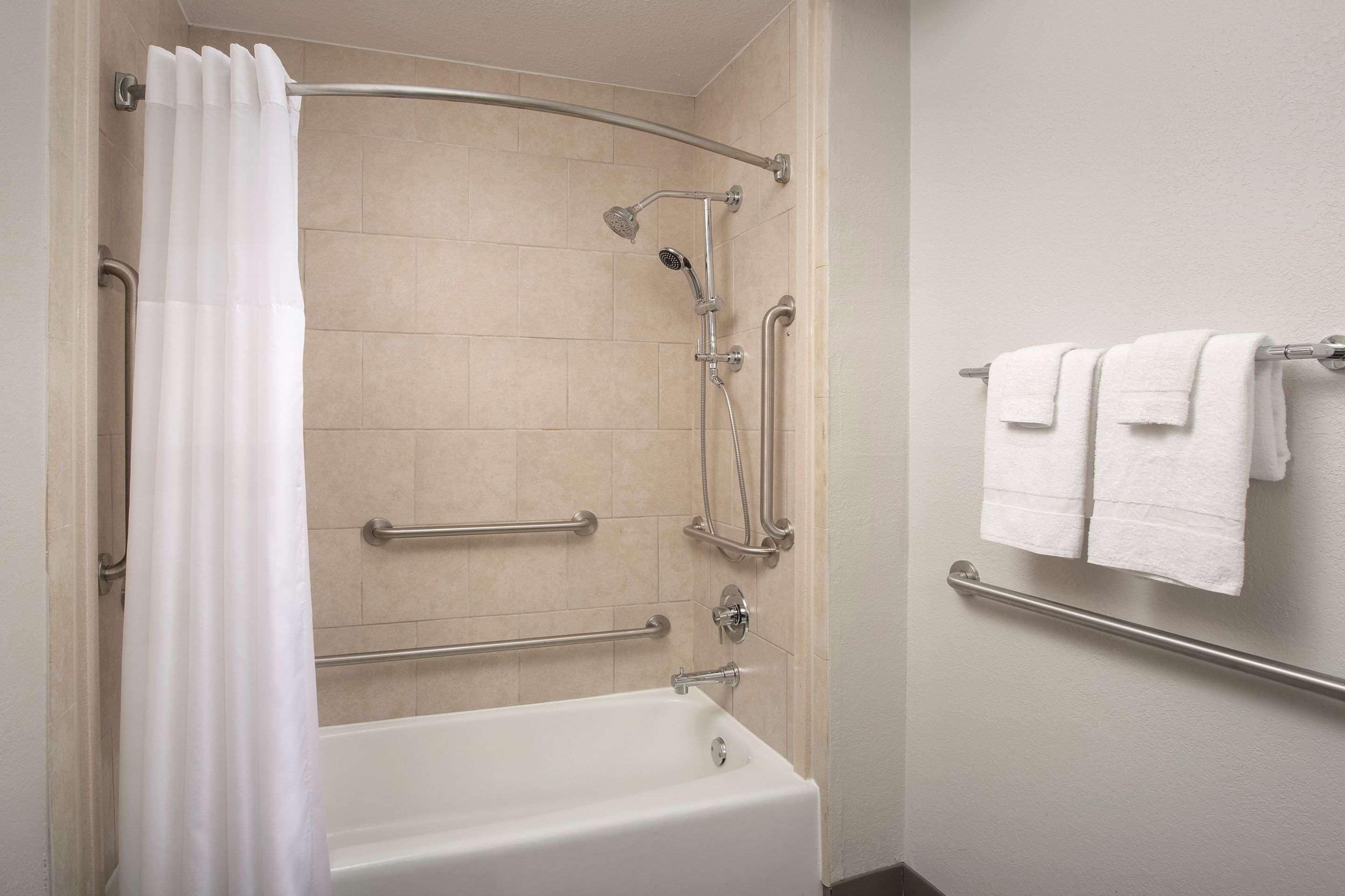 Un baño moderno con bañera, ducha, barras de apoyo y un perchero para toallas.