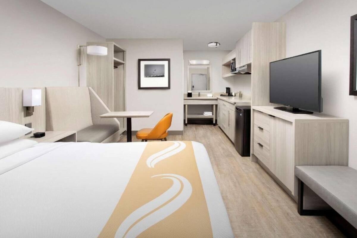 Habitación de hotel con cama, escritorio, silla, televisión, baño y una pequeña kitchenette.
