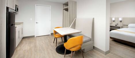 Habitación de hotel compacta con kitchenette, cama, escritorio con dos sillas y un pequeño rincón de estar.