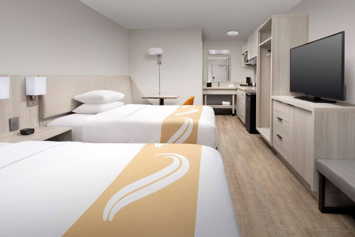 Habitación de hotel con dos camas, televisor, escritorio y baño.