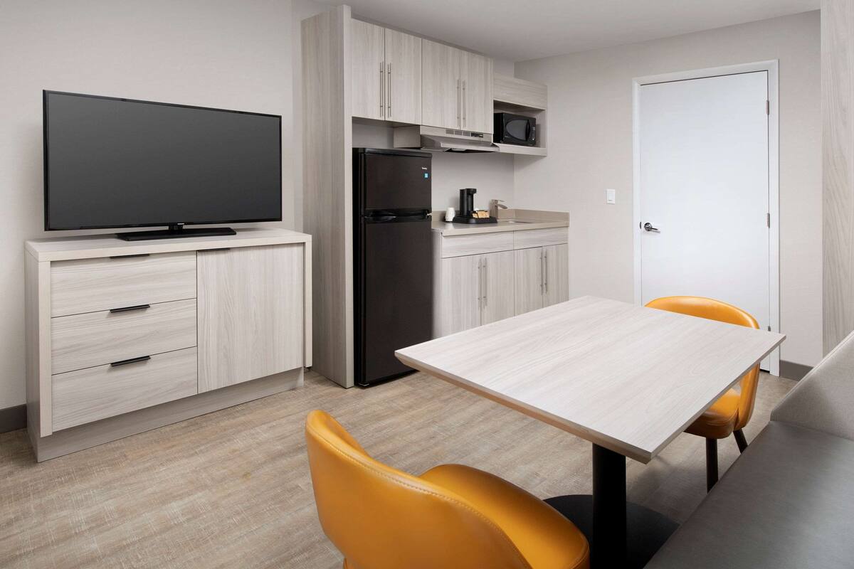 Una cocina moderna con televisor de pantalla plana, refrigerador y microondas. Hay una mesa de comedor con dos sillas.