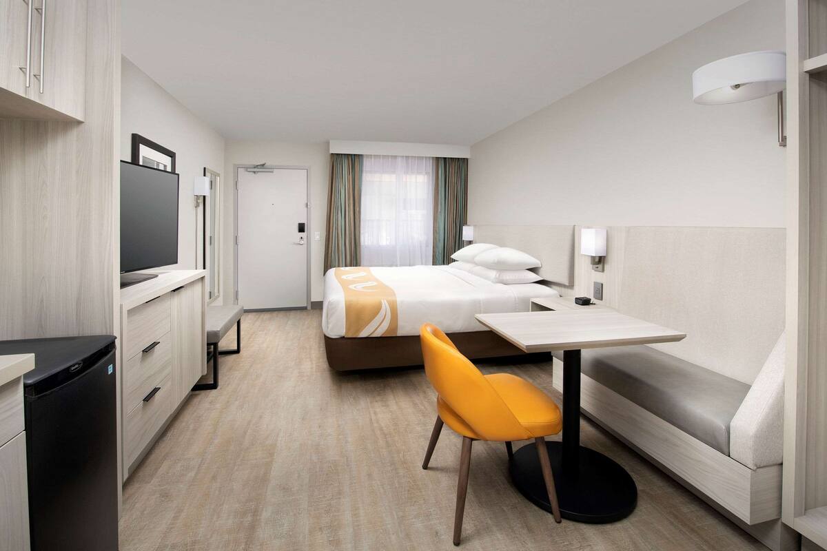 Una habitación de hotel con cama, escritorio, silla, televisor y minibar.
