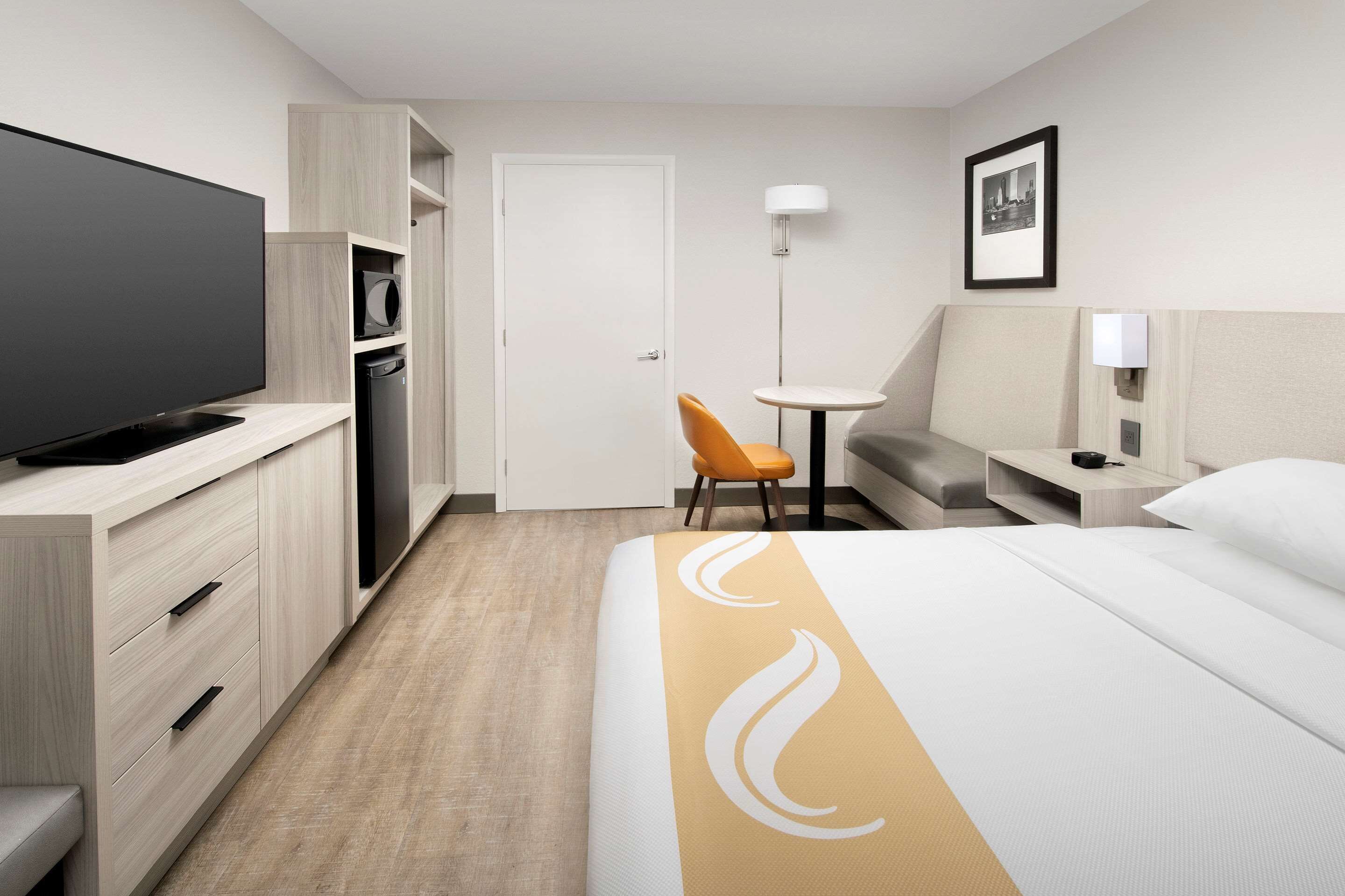 A hotel room with a bed, a TV, a desk, a chair, a wardrobe, and a door.