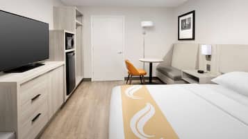 A hotel room with a bed, a TV, a desk, a chair, a wardrobe, and a door.