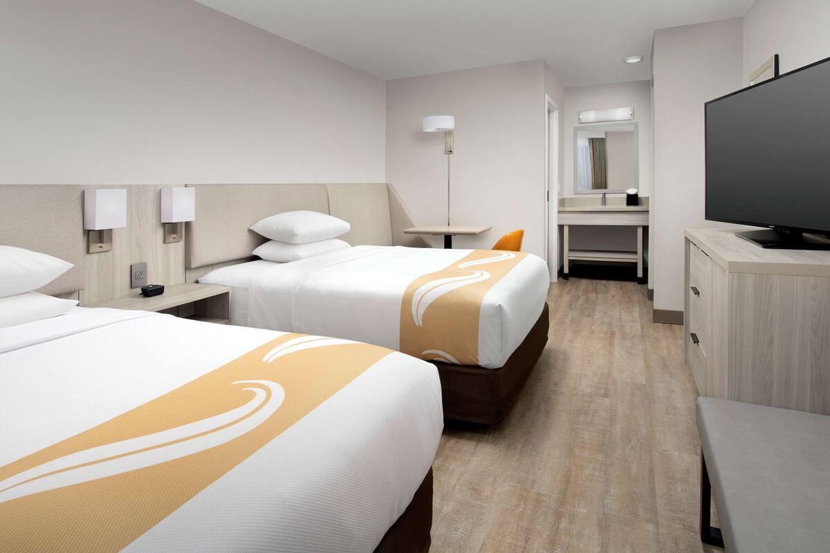 Una habitación de hotel con dos camas, televisión, escritorio y espejo.