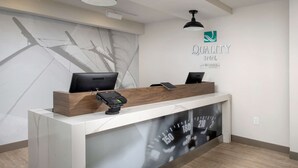 Un comptoir d’accueil d’hôtel doté d’un écran numérique, d’un comptoir en bois et d’un logo affiché sur le mur.