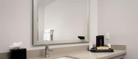 Un baño con un lavabo blanco, un espejo, un dispensador de jabón negro y un dispensador de toallas.