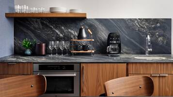Uma cozinha moderna com bancada de mármore, armários de madeira, máquina de café e forno embutido.