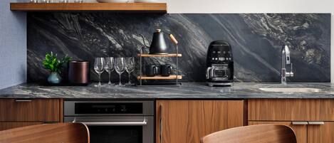 A modern kitchen with a marble countertop, wooden cabinets, a coffee machine, and a built-in oven.