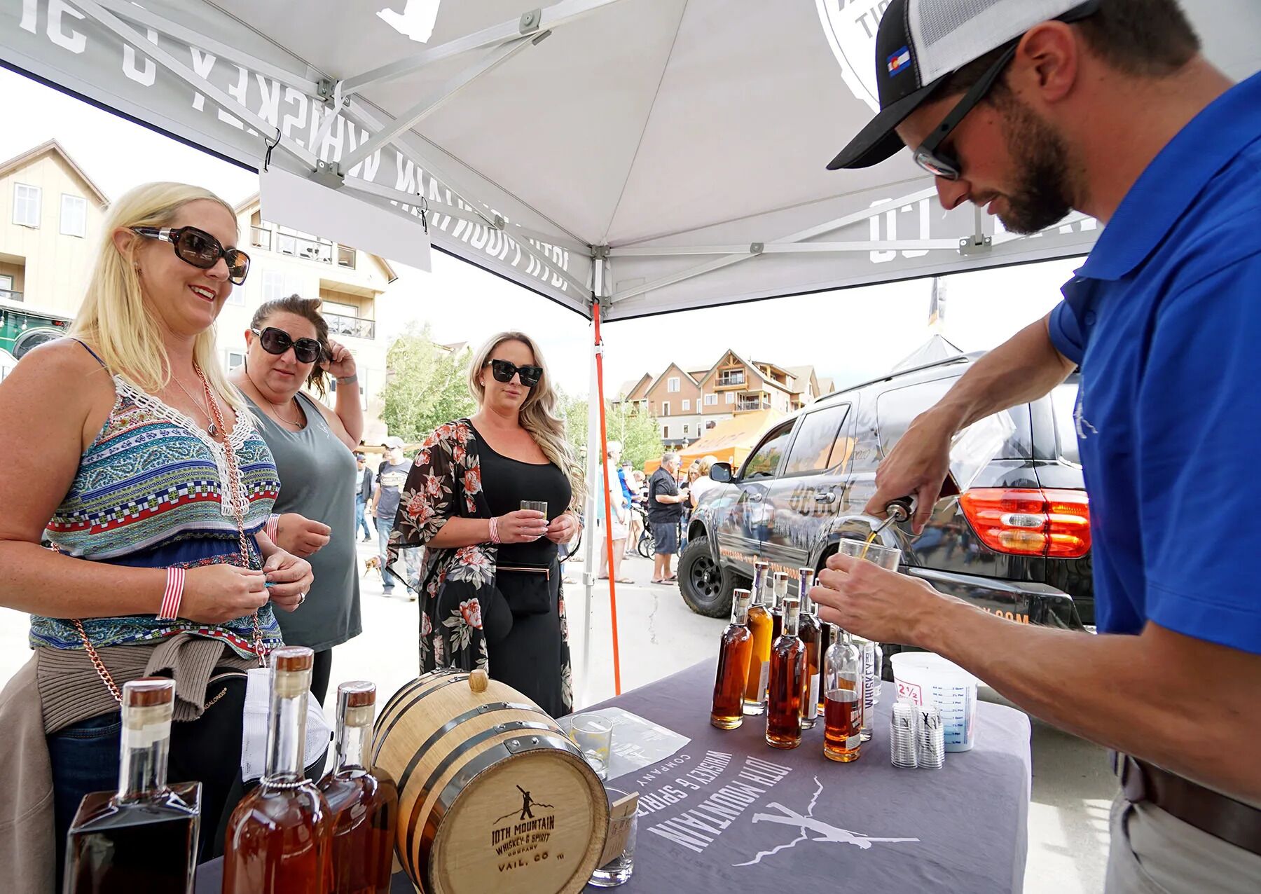 A group of people at an outdoor event with a table displaying various bottles and a wooden barrel.