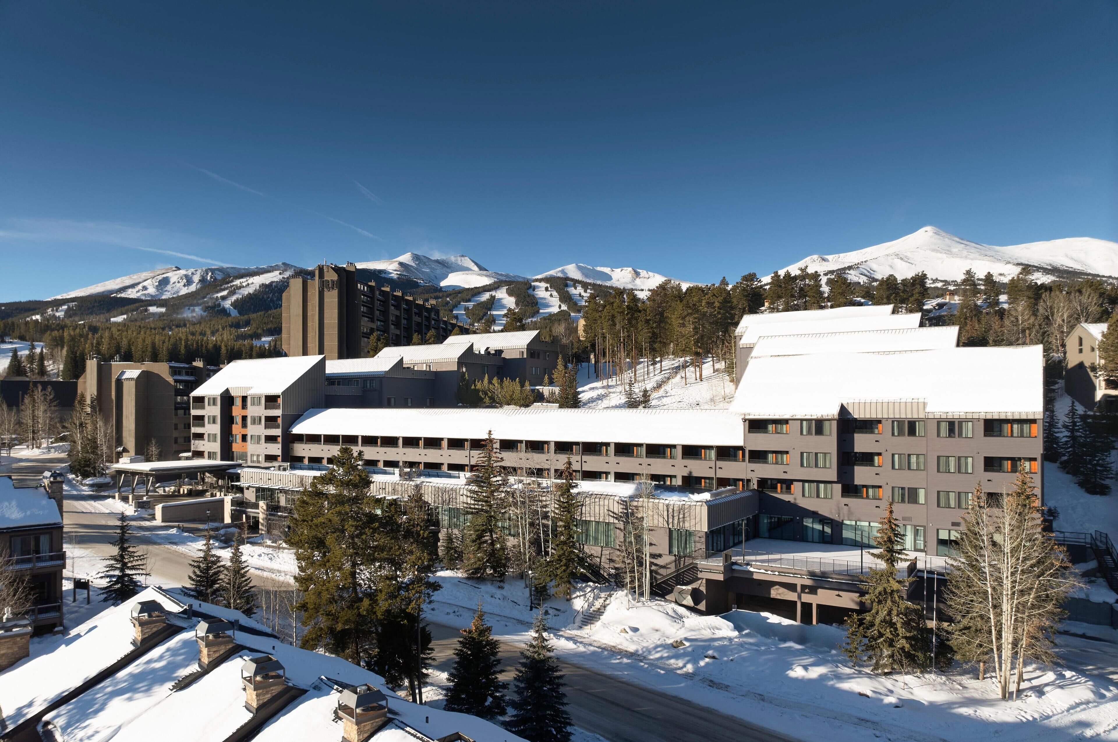 A hotel with multiple buildings, snow-covered surroundings, and a mountain backdrop.