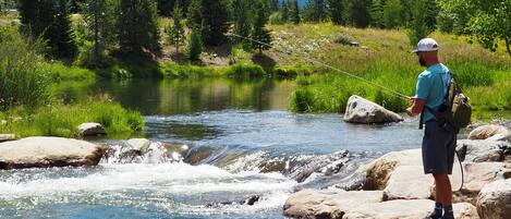 A man fishing by a river with a mountain in the background.