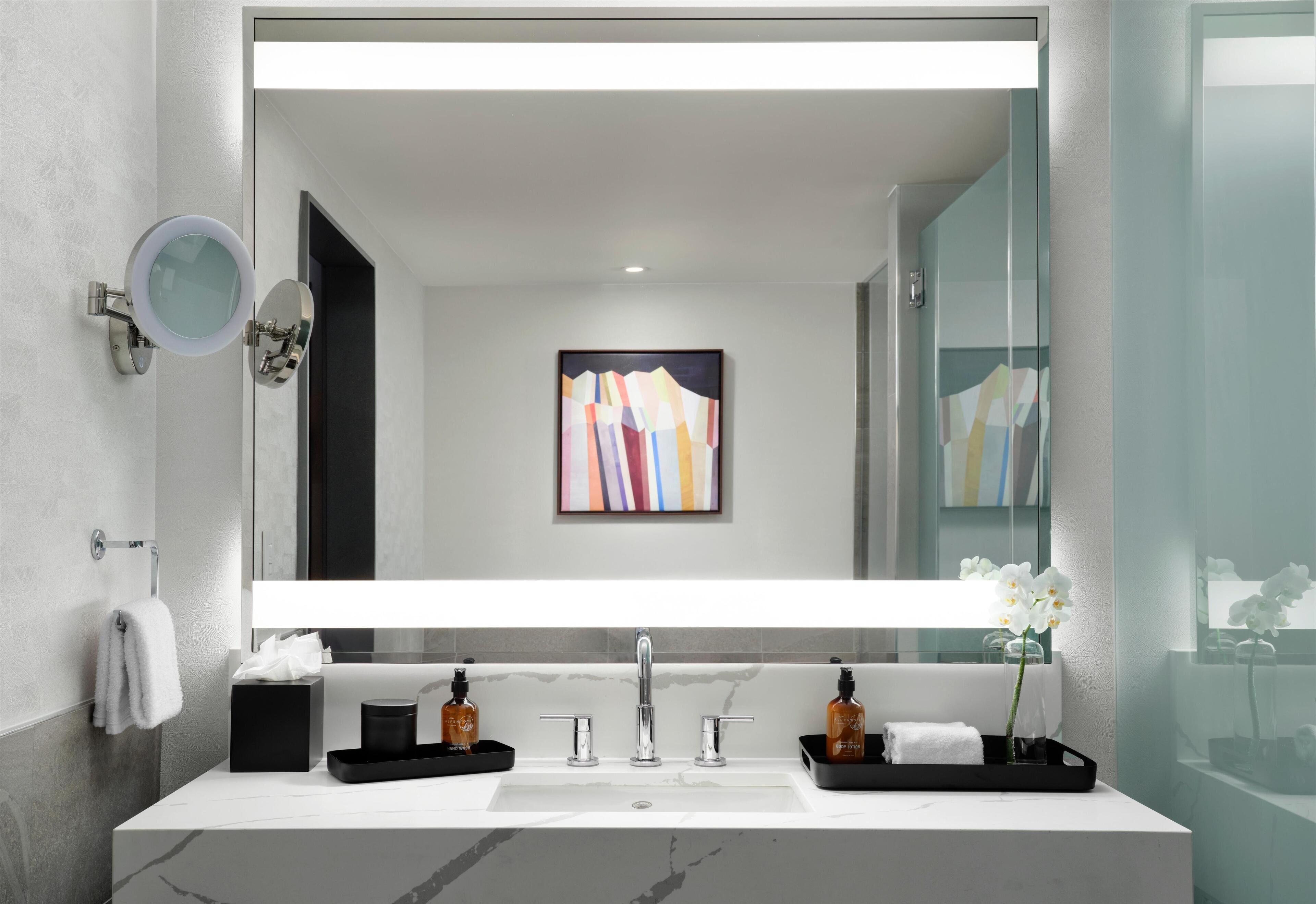 Un baño moderno con un espejo grande, un lavabo blanco y una cabina de ducha de vidrio.