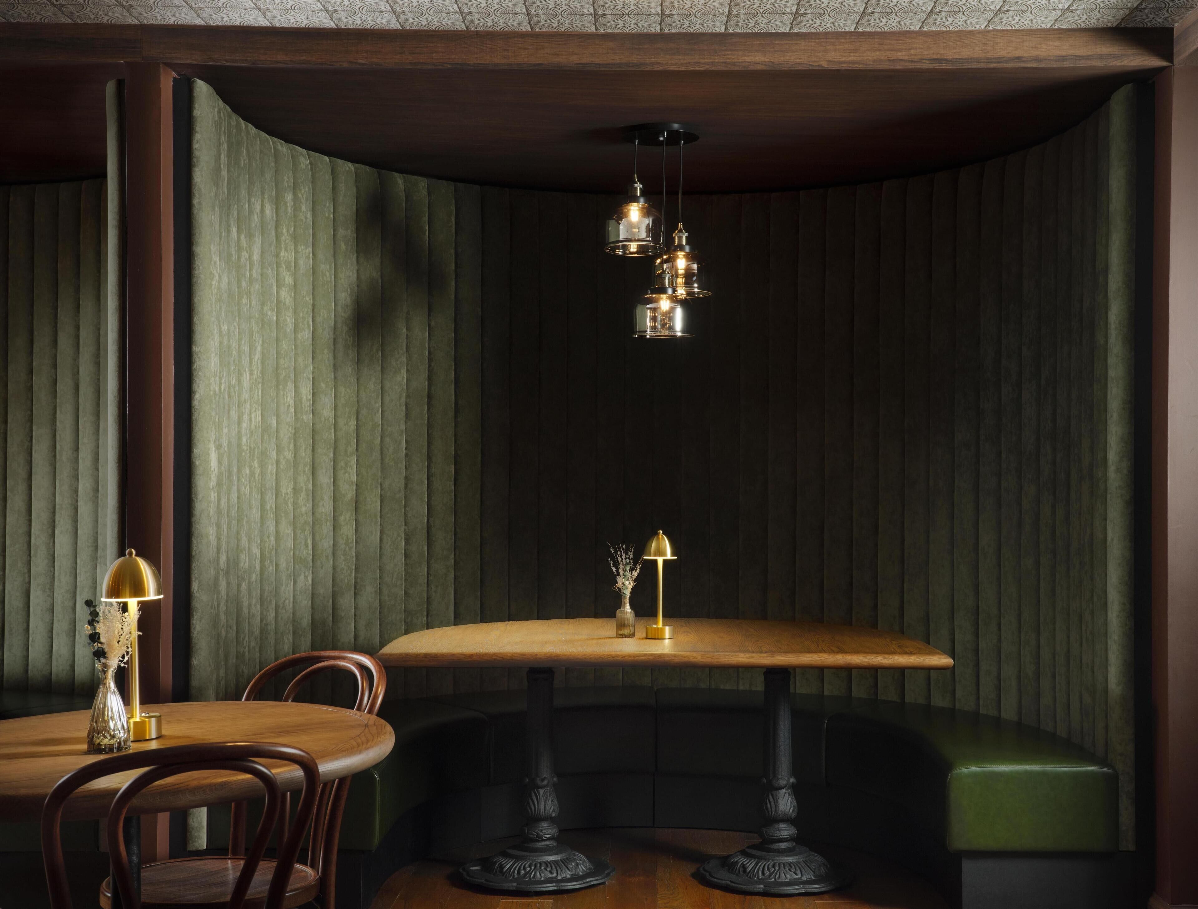 Un rincón acogedor con una mesa y sillas de madera, un banco tapizado de verde y una lámpara decorativa.