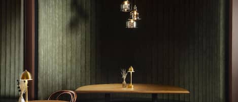 Un rincón acogedor con una mesa y sillas de madera, un banco tapizado de verde y una lámpara decorativa.