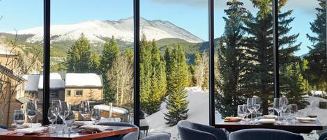 Ein Restaurant mit großen Fenstern und Blick auf einen schneebedeckten Berg und Kiefern.