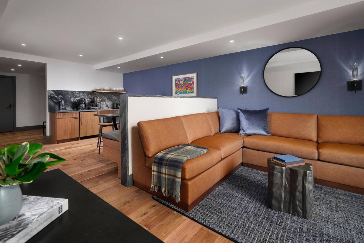 A modern living room with a brown sectional sofa, a coffee table, and a dining area with a kitchen in the background.