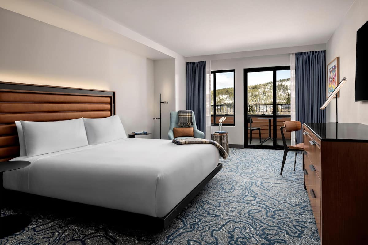 A hotel room with a large bed, a desk, a chair, a dresser, and a balcony with a view of the outdoors.