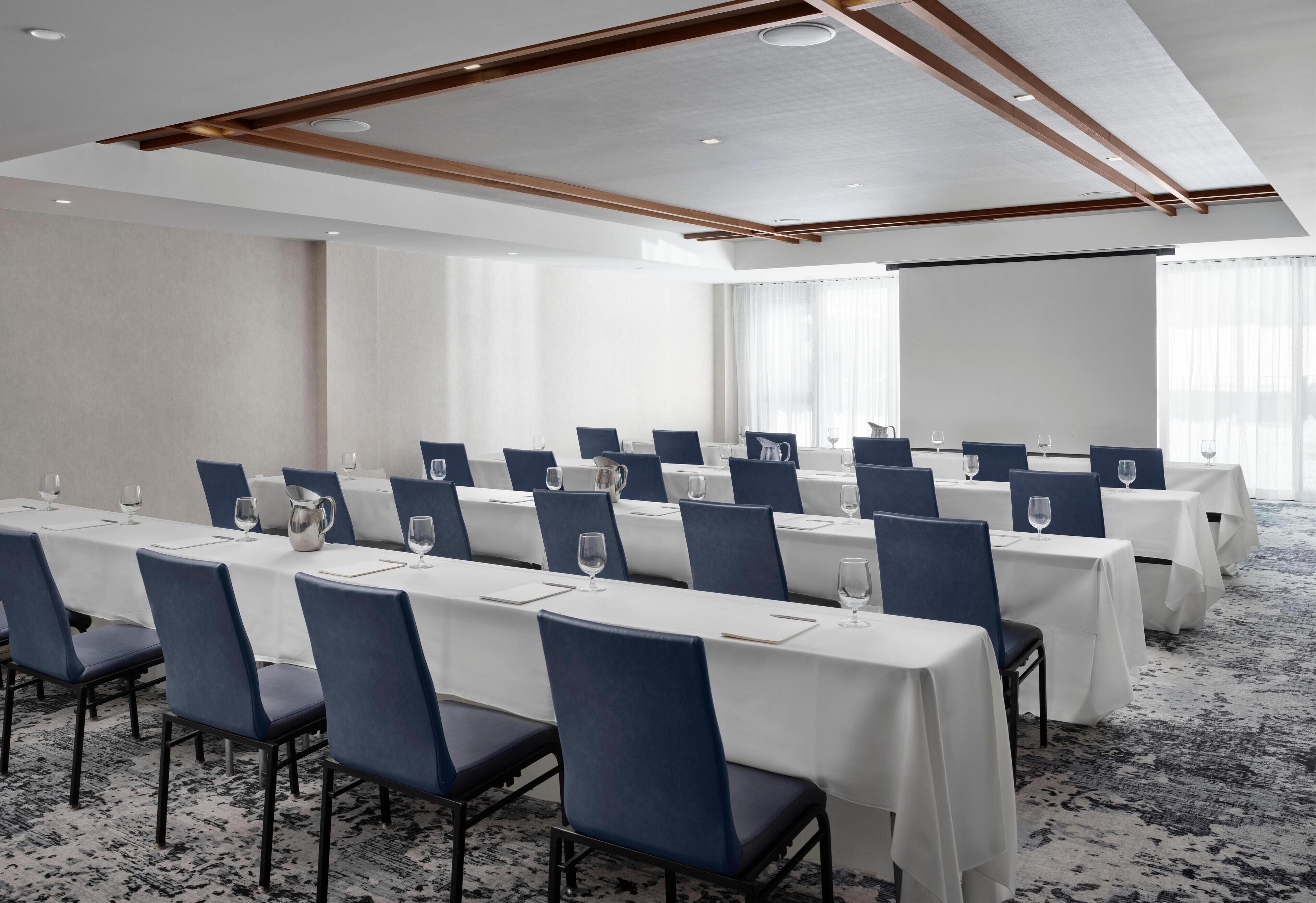 A conference room with rows of tables and chairs, white tablecloths, and a carpeted floor.