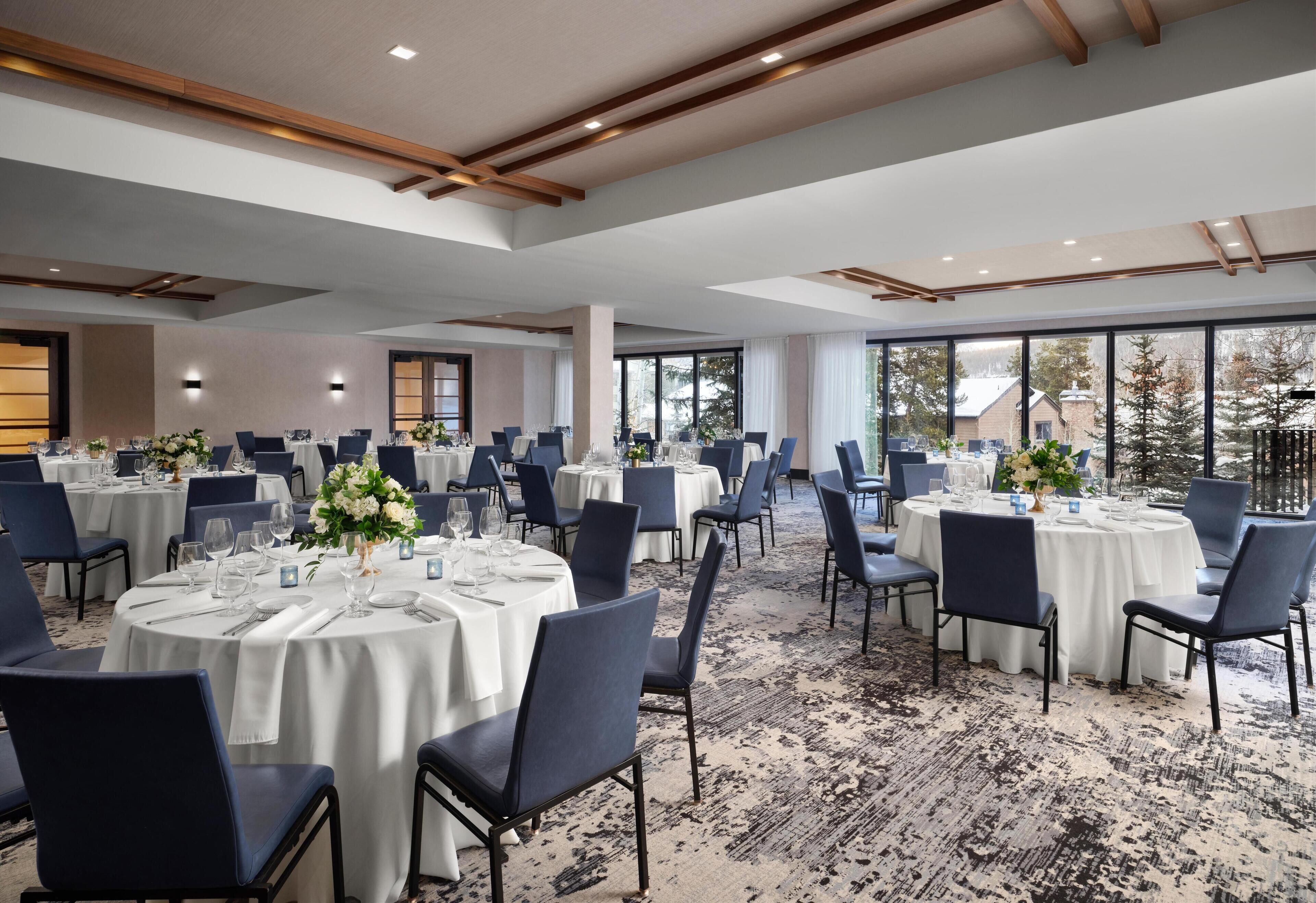 A large banquet hall with round tables, blue chairs, and white tablecloths.