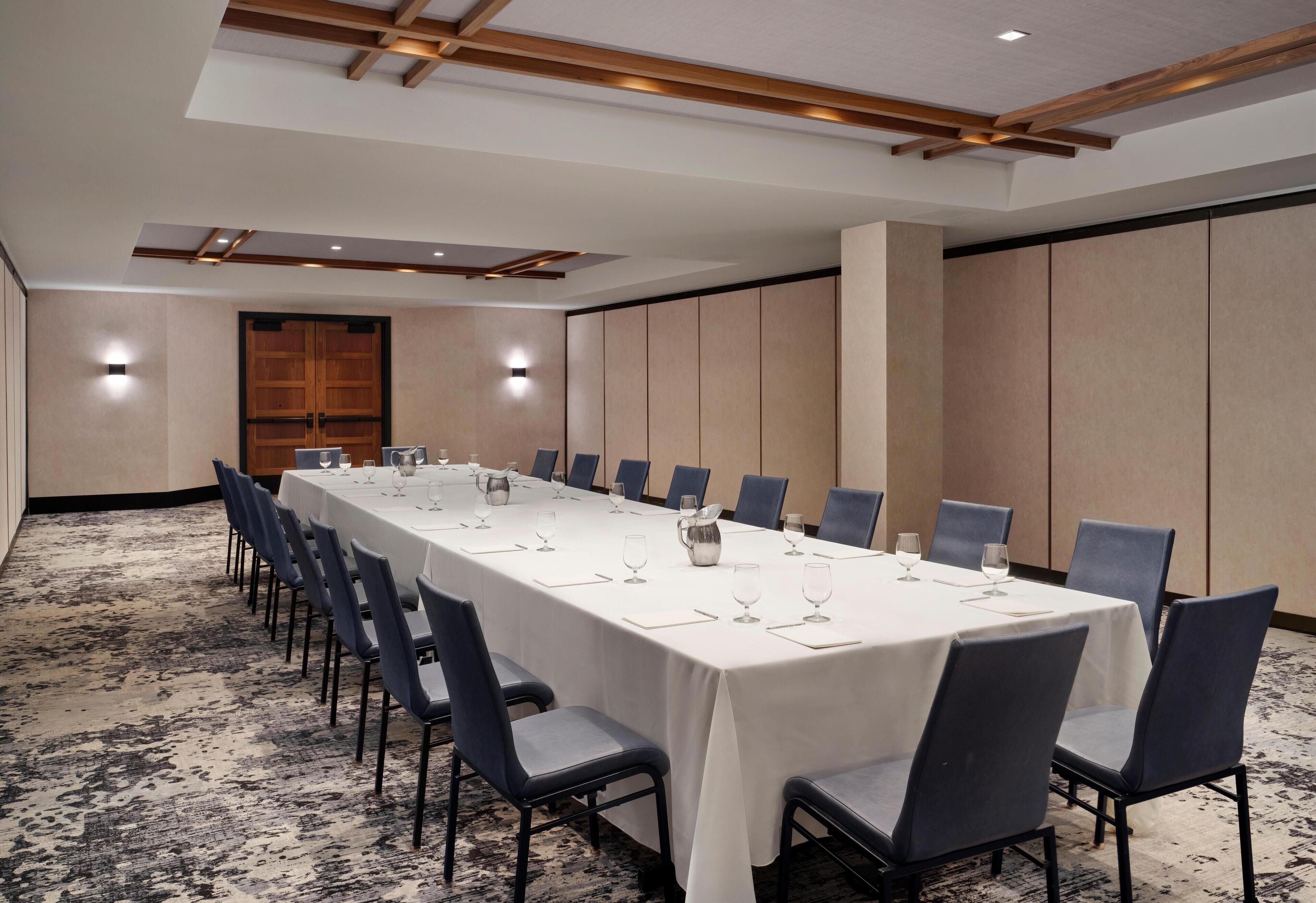 Een vergaderzaal met een lange tafel, stoelen en een vloerbedekking.
