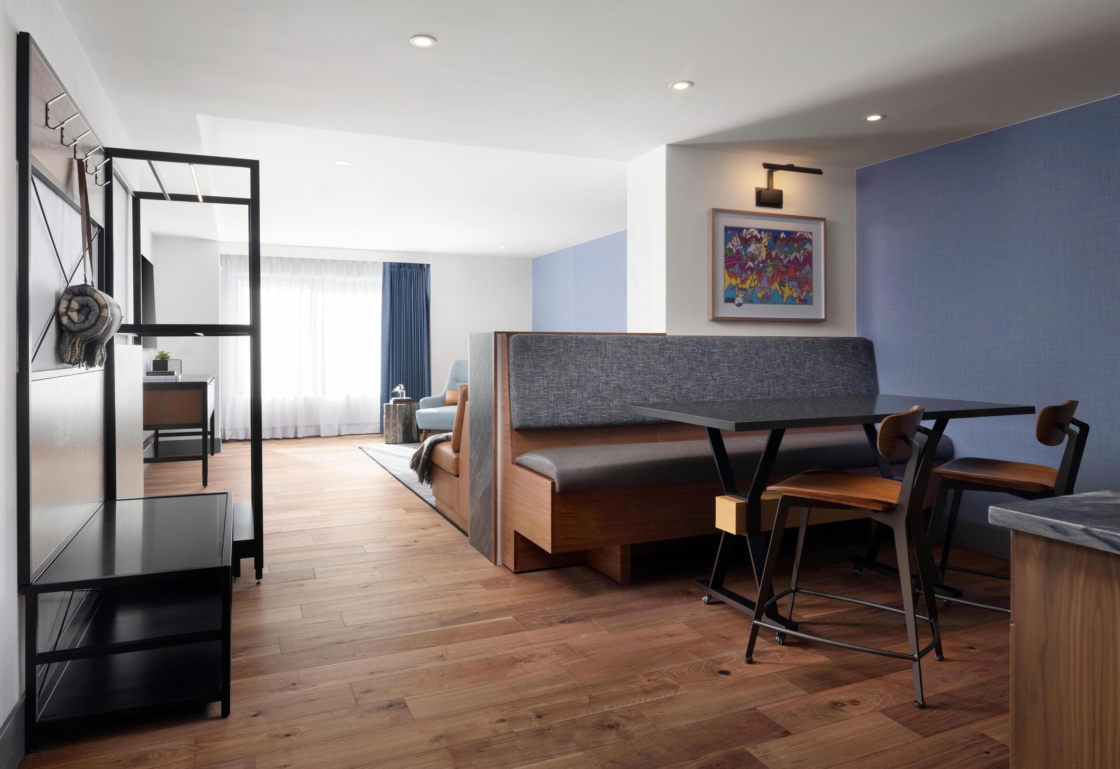 A modern living room with a sofa, a dining table, and chairs. There is a wooden floor, a blue wall, and a framed picture on the wall.
