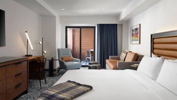 A hotel room with a bed, a desk, a chair, a sofa, a TV, and a view of the outside.