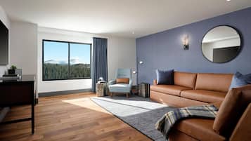 A modern living room with a brown leather sofa, a round mirror, and a large window offering a mountain view.