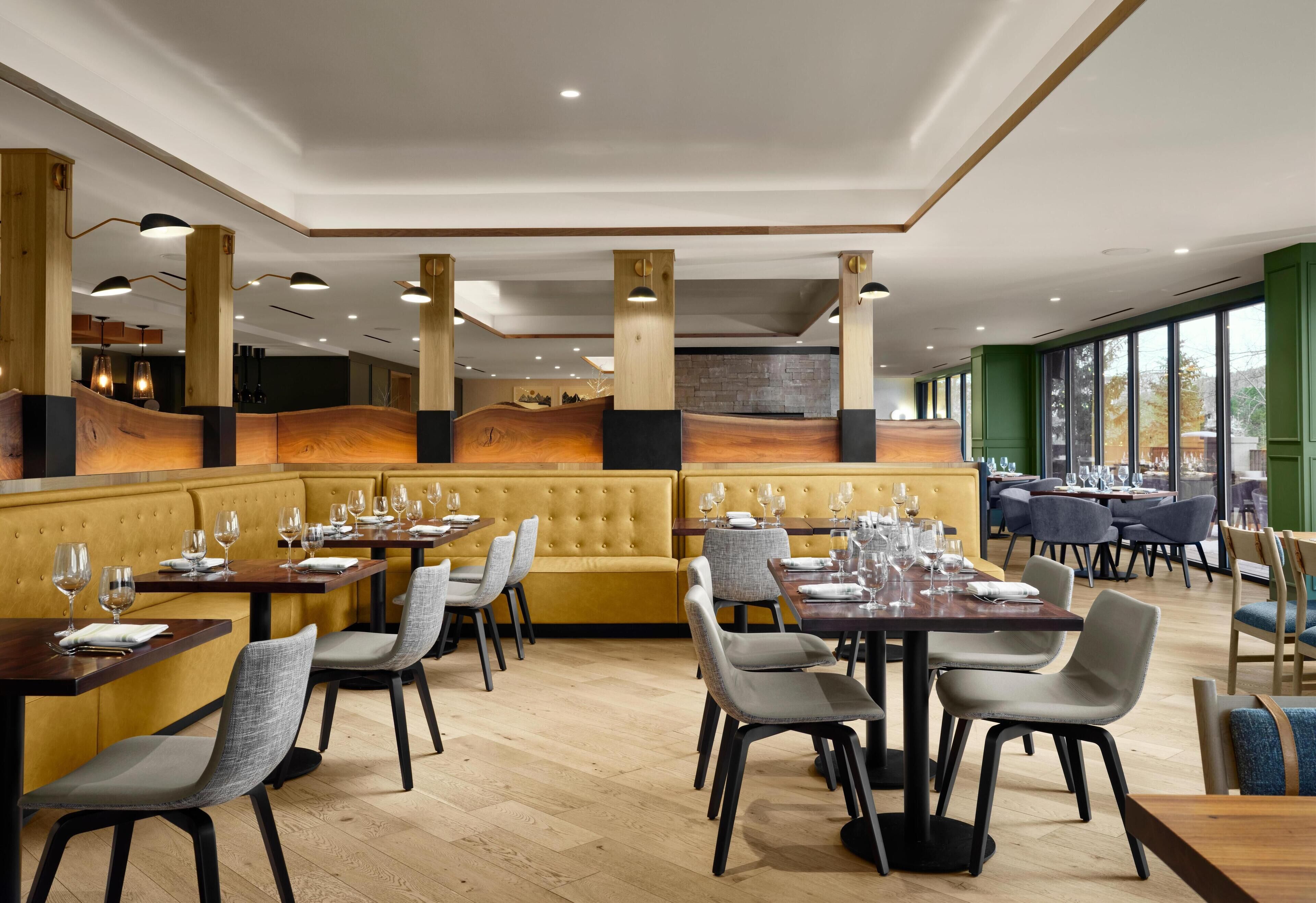 A restaurant with wooden accents, cushioned seating, and a view of the outdoors. Tables are set with wine glasses and plates.