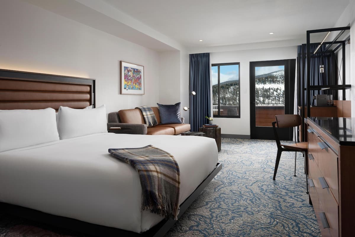 A modern hotel room with a large bed, a sofa, a desk, and a view of a snowy mountain.