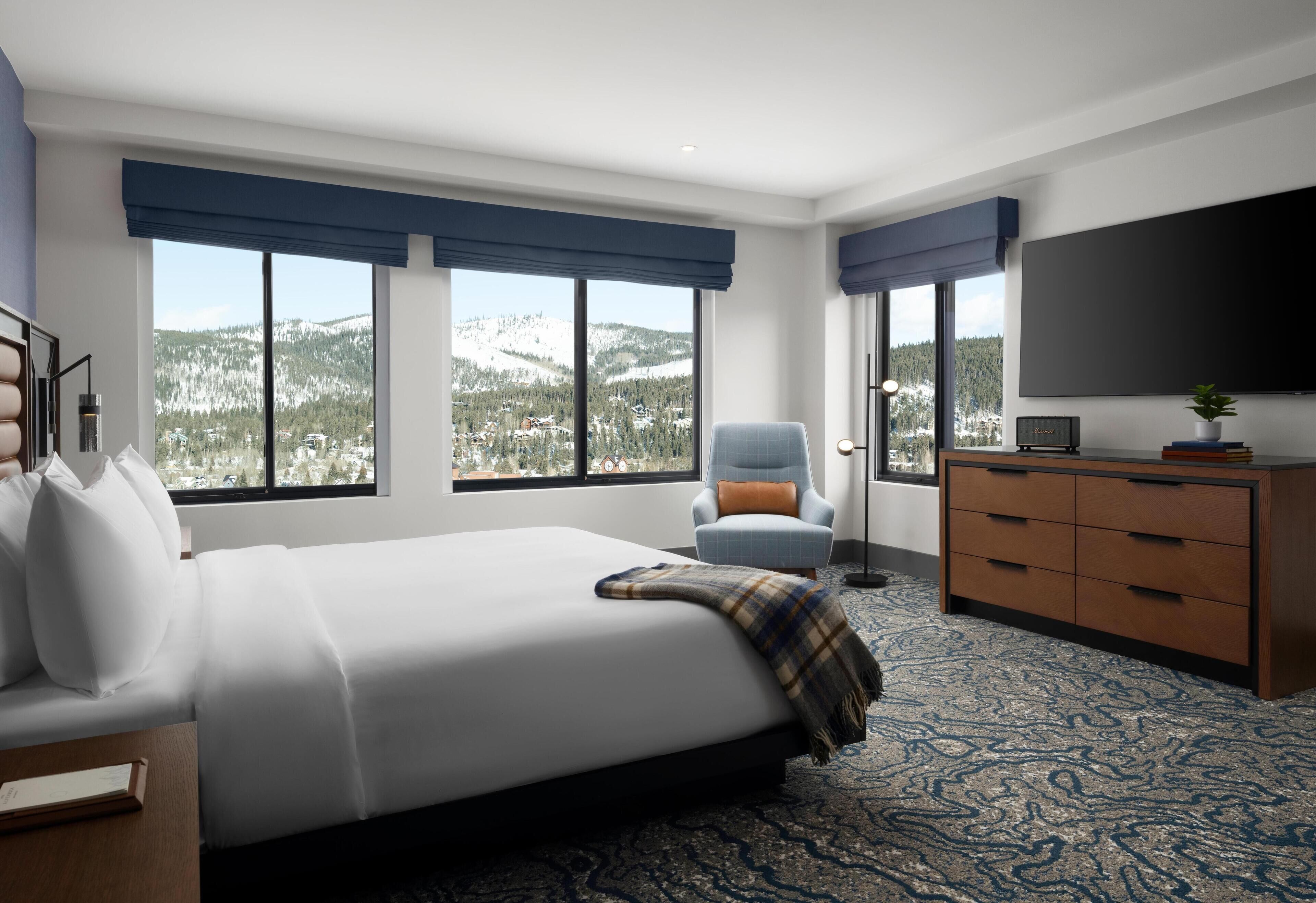 A modern hotel room with a large bed, a chair, a dresser, and a TV.