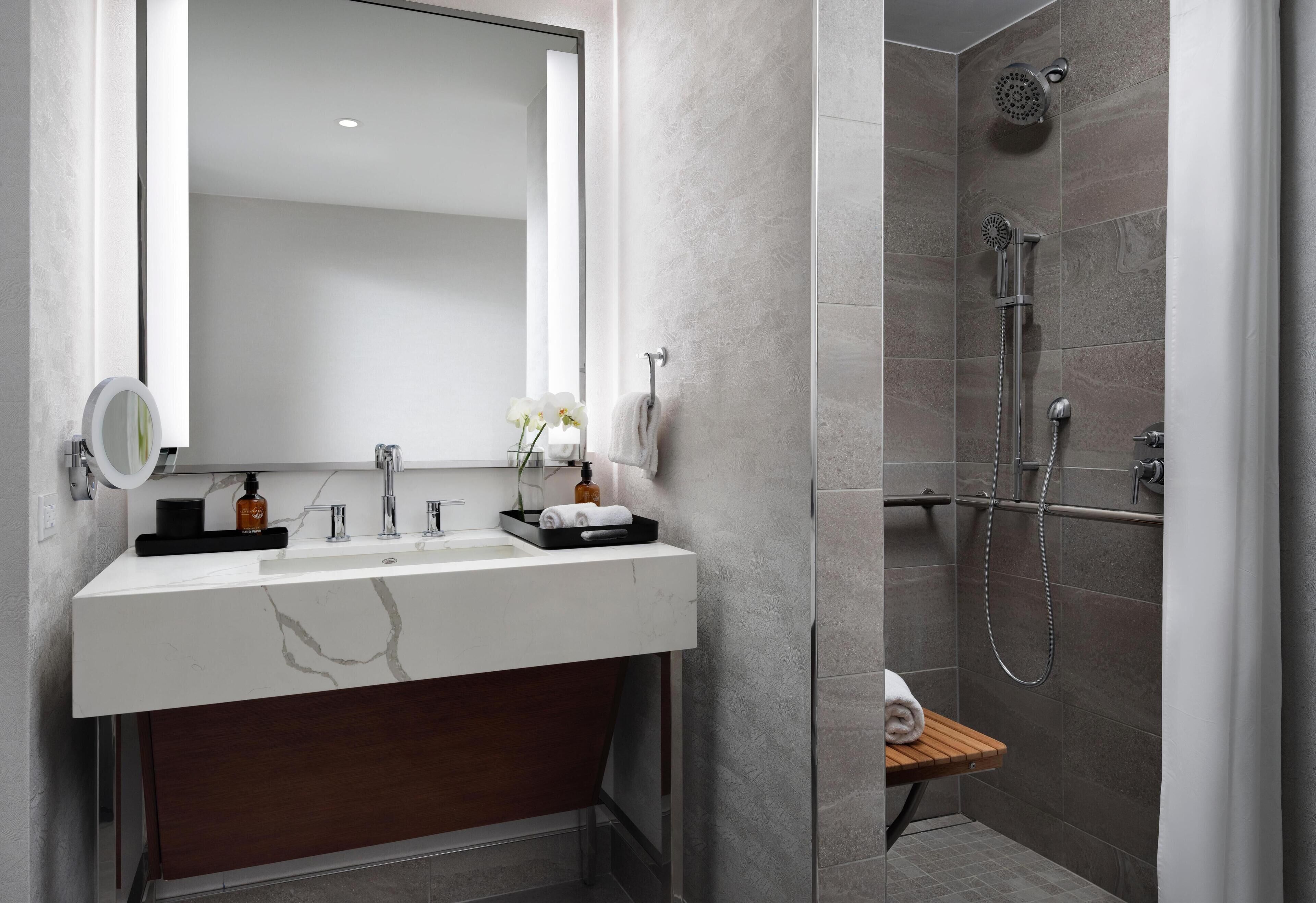 A modern bathroom with a marble sink, a wooden vanity, a large mirror, and a shower area.