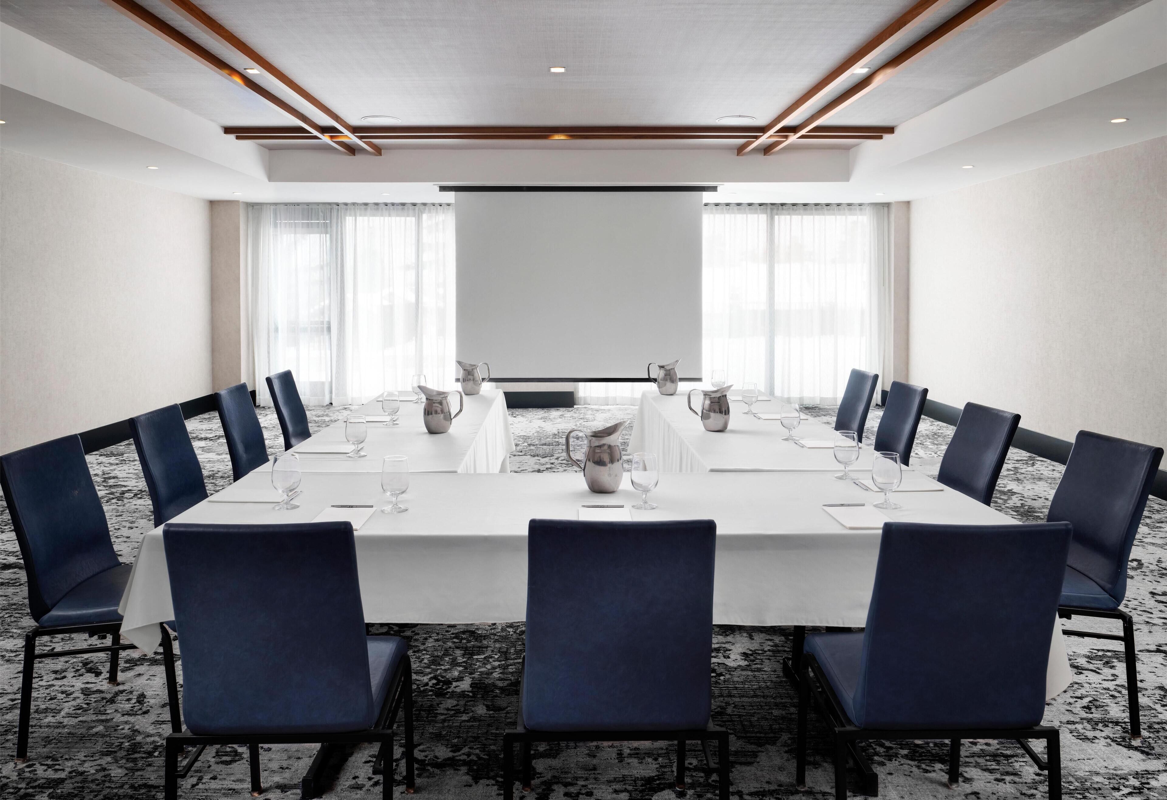 A conference room with a long table, blue chairs, and a projector screen.