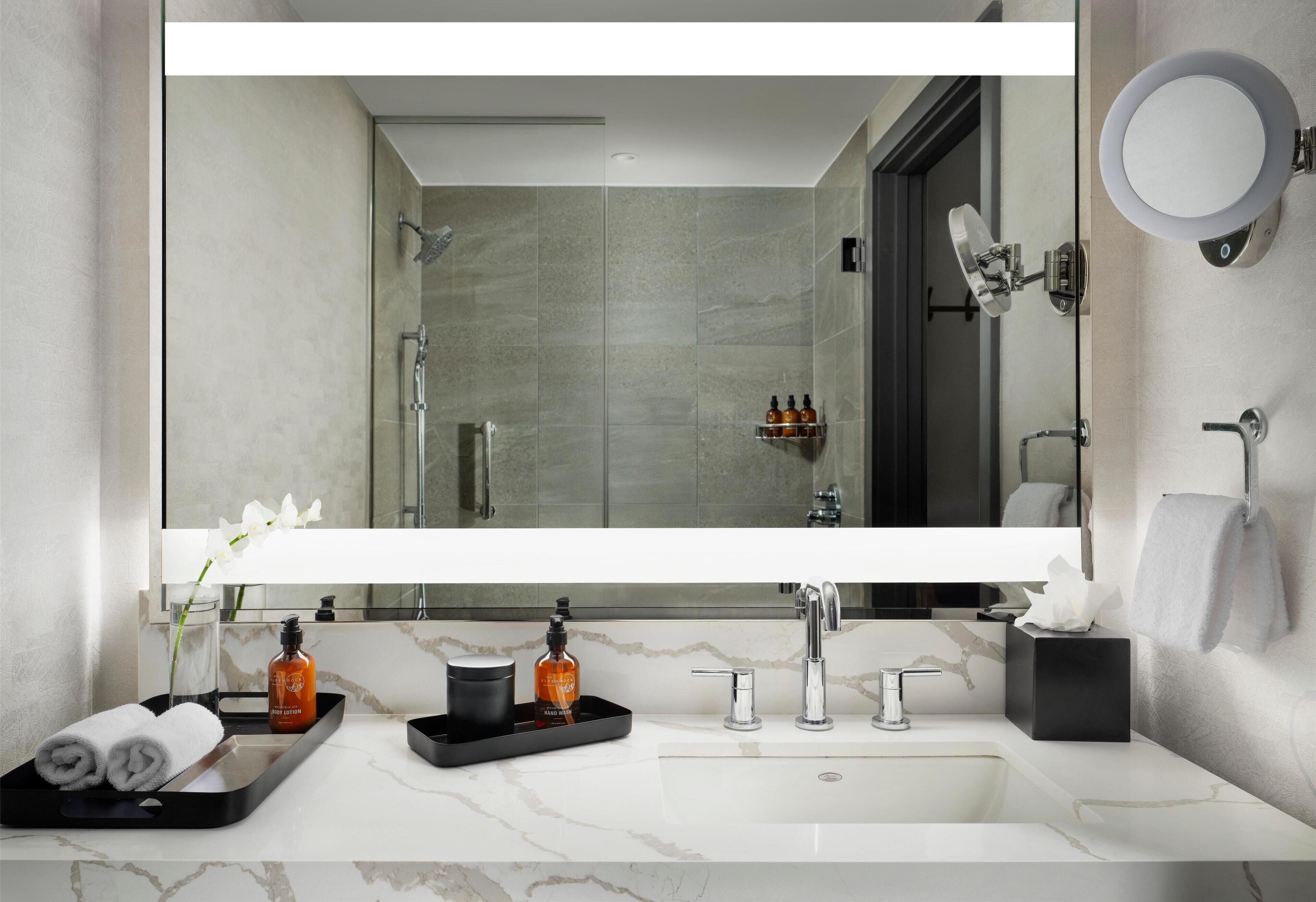 A modern bathroom with a large mirror, a sink, and a shower.