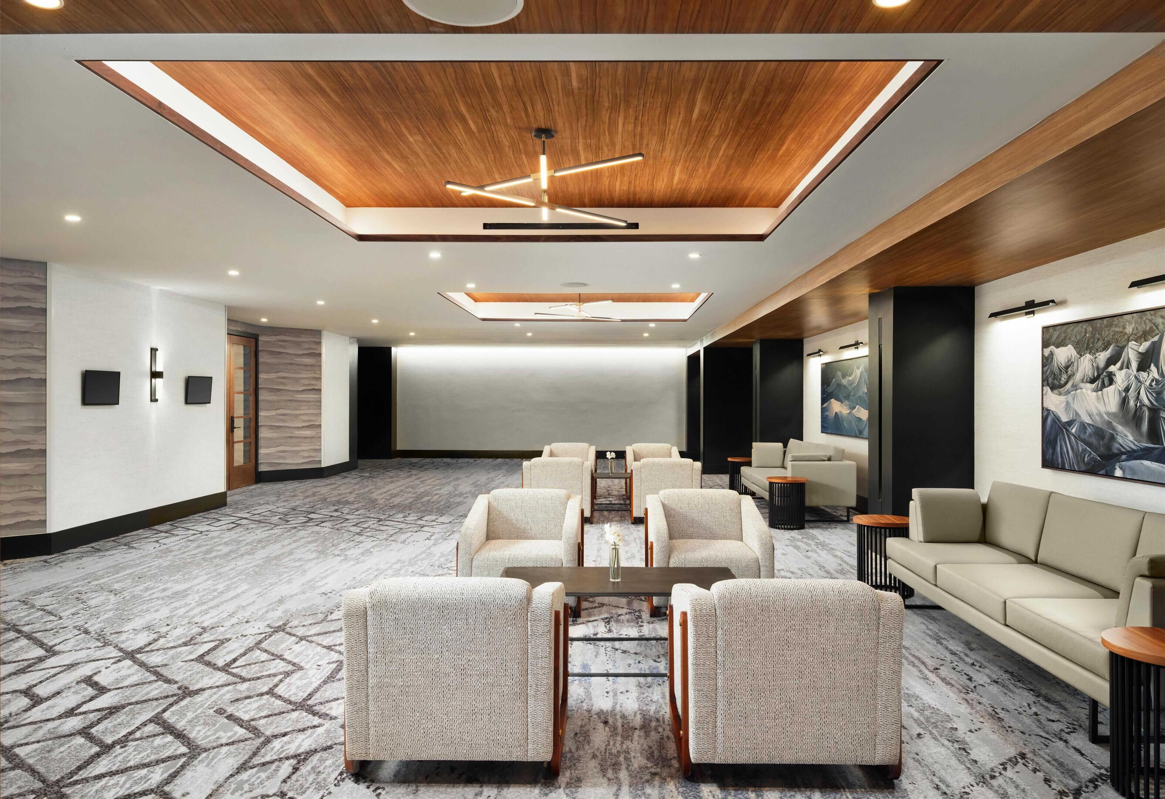 Une salle de conférence spacieuse, dotée d’un plafond haut, d’un éclairage moderne et d’un tapis à motifs.