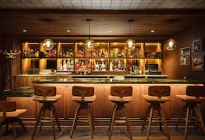 Eine Bar mit Holzhocker, einer Auswahl an Spirituosenflaschen und hängenden Pendelleuchten.