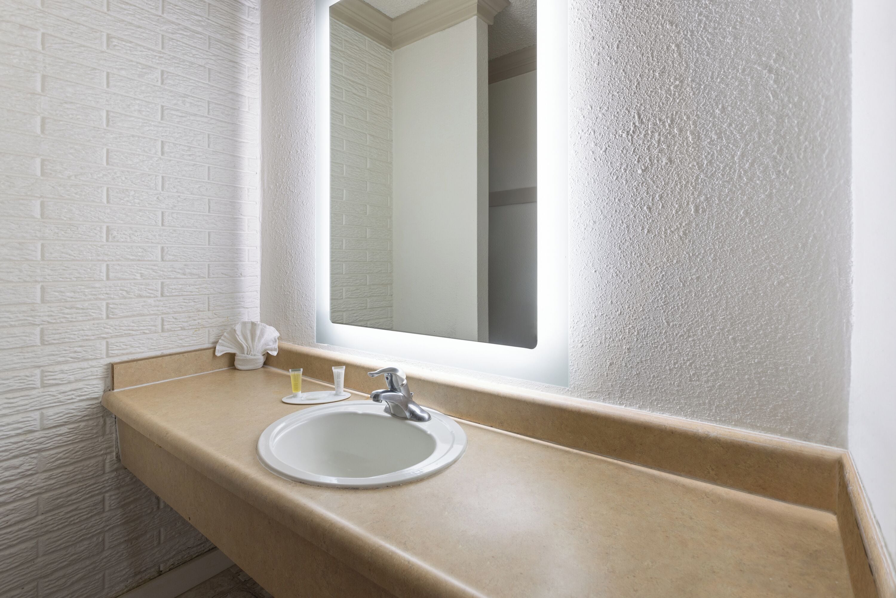 A bathroom with a white brick wall, a beige countertop, a white sink, and a mirror.