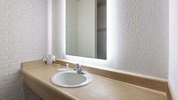 Een badkamer met een witte baksteenmuur, een beige aanrechtblad, een witte wastafel en een spiegel.