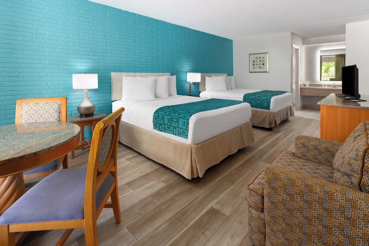 A hotel room with two beds, a desk, a chair, and a television.