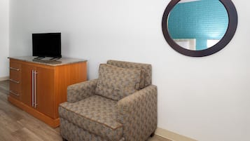 Una habitación con un armario de madera, un sillón estampado y un espejo redondo en la pared.