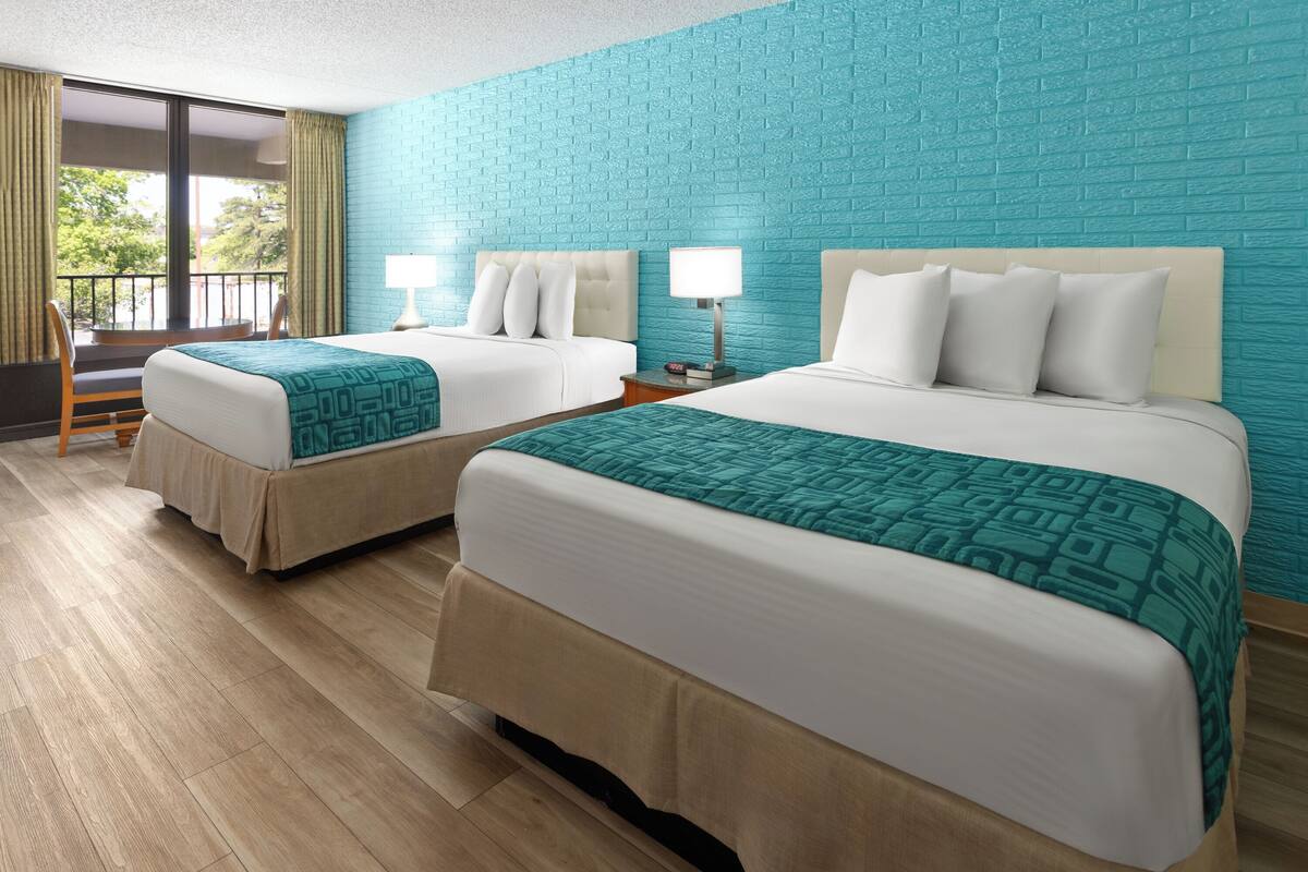 A hotel room with two beds, a balcony with a view, and a blue brick wall.