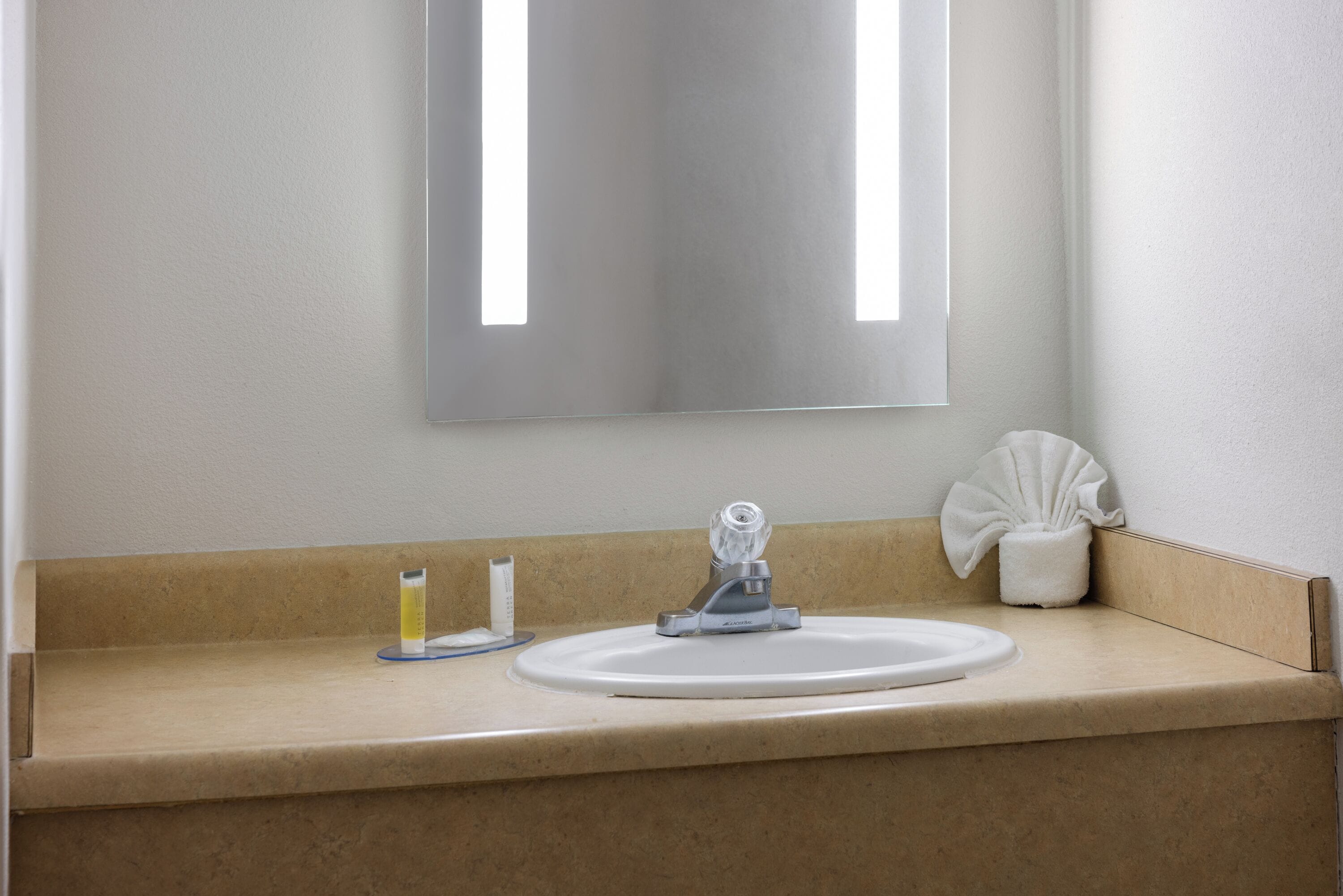 A bathroom with a beige countertop, a white sink, a mirror, and a tissue holder.