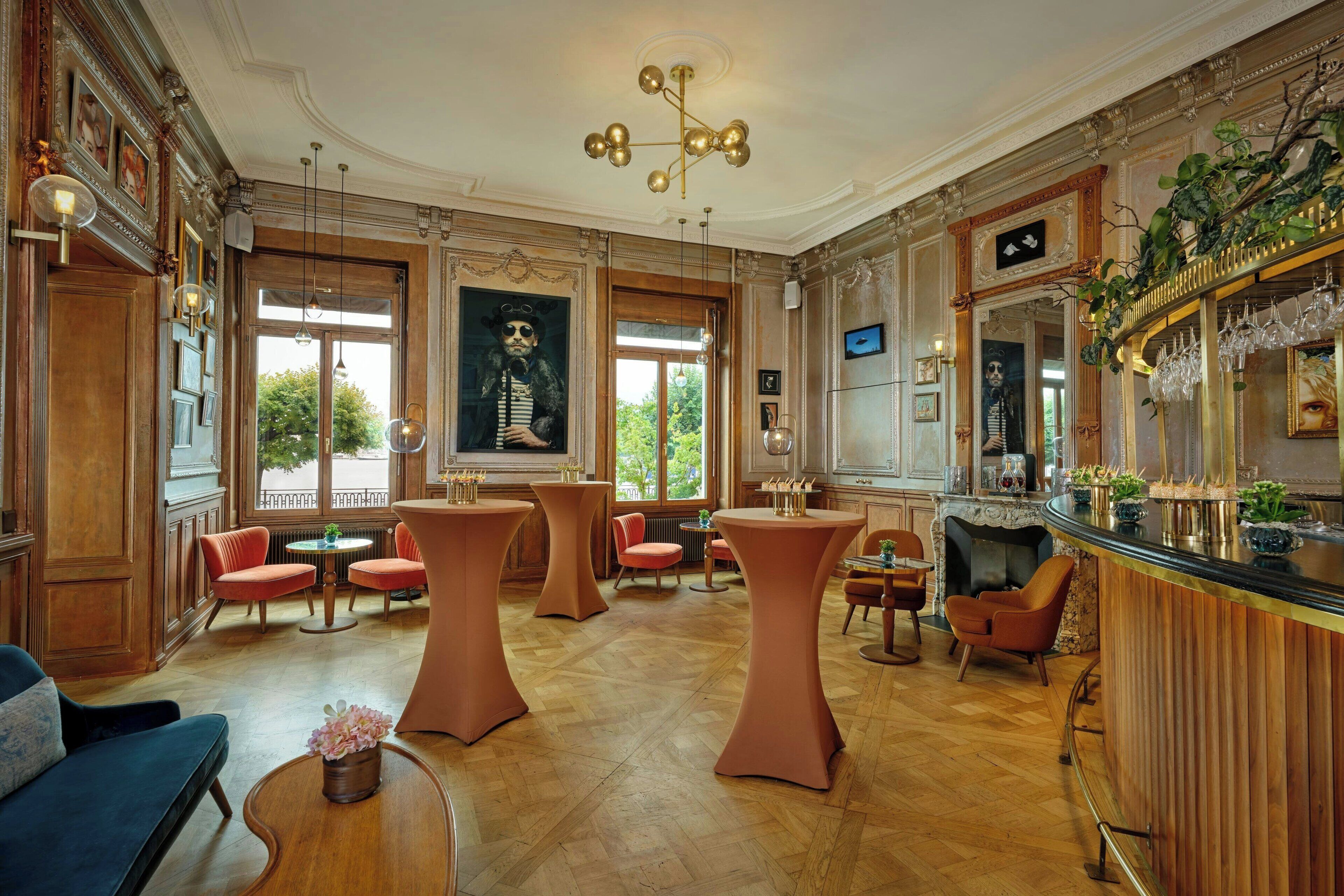 A spacious room with high ceilings, ornate wood paneling, and a large window offering a view of greenery.
