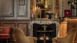 A room with a fireplace, two armchairs, a round table, and a mirror above the fireplace.