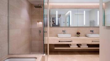 Un baño moderno con cabina de ducha de vidrio, dos lavamanos y un espejo grande.