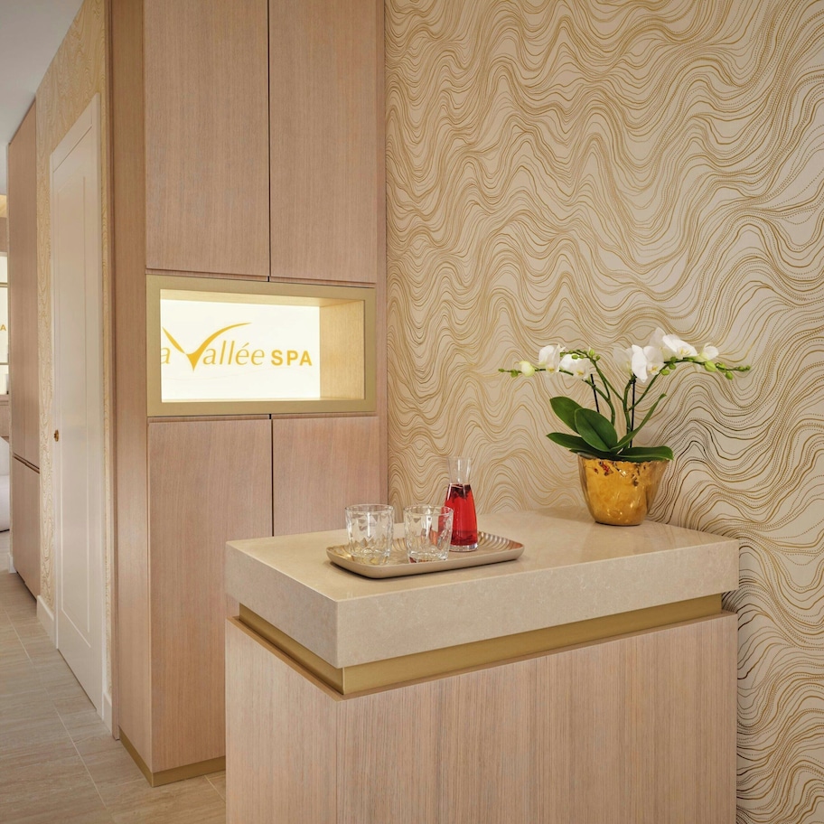 A reception area with a wooden reception desk, a sign reading "La Vallée SPA", and a potted orchid.