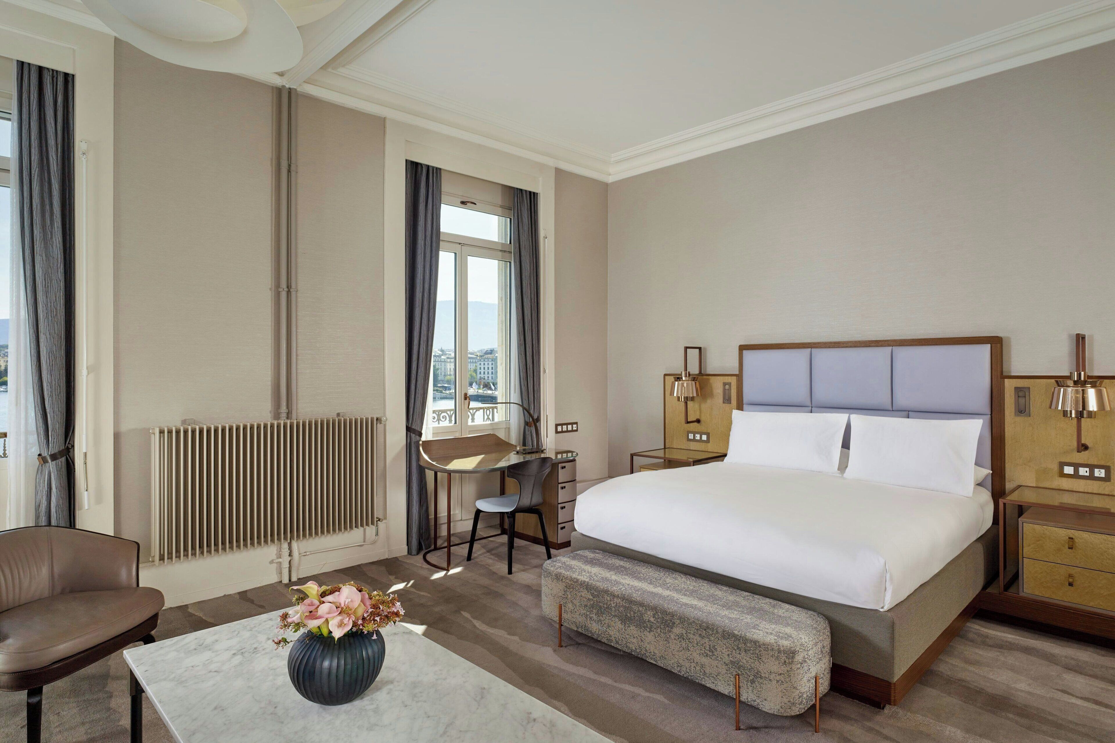 Habitación de hotel con una cama grande, un escritorio, una silla, una mesita con un florero y un radiador.