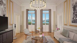 A spacious living room with a large TV, comfortable seating, a decorative table, and a view of a body of water through large windows.