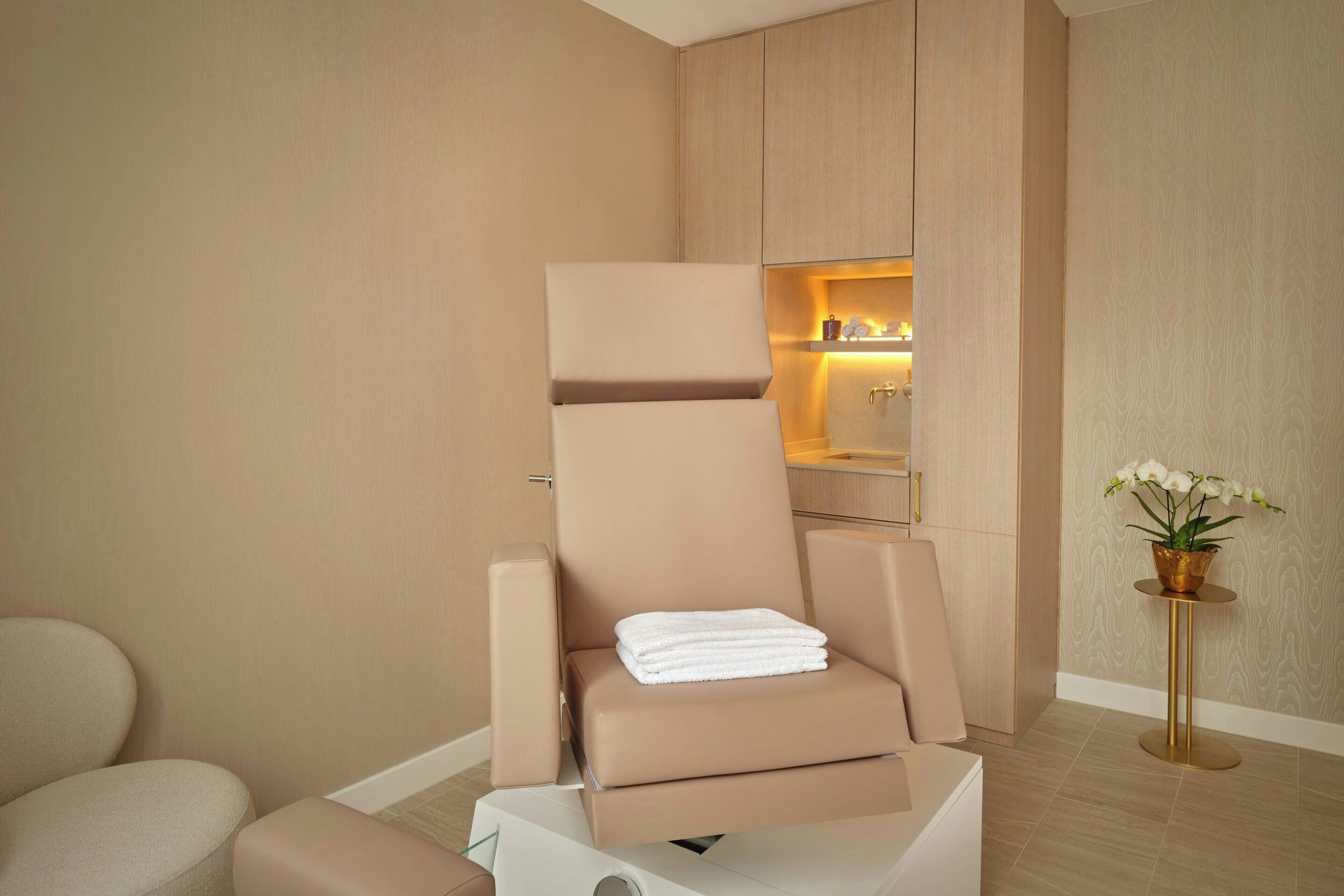 A modern spa room with a massage chair, a small table with a plant, and a shelf with candles.