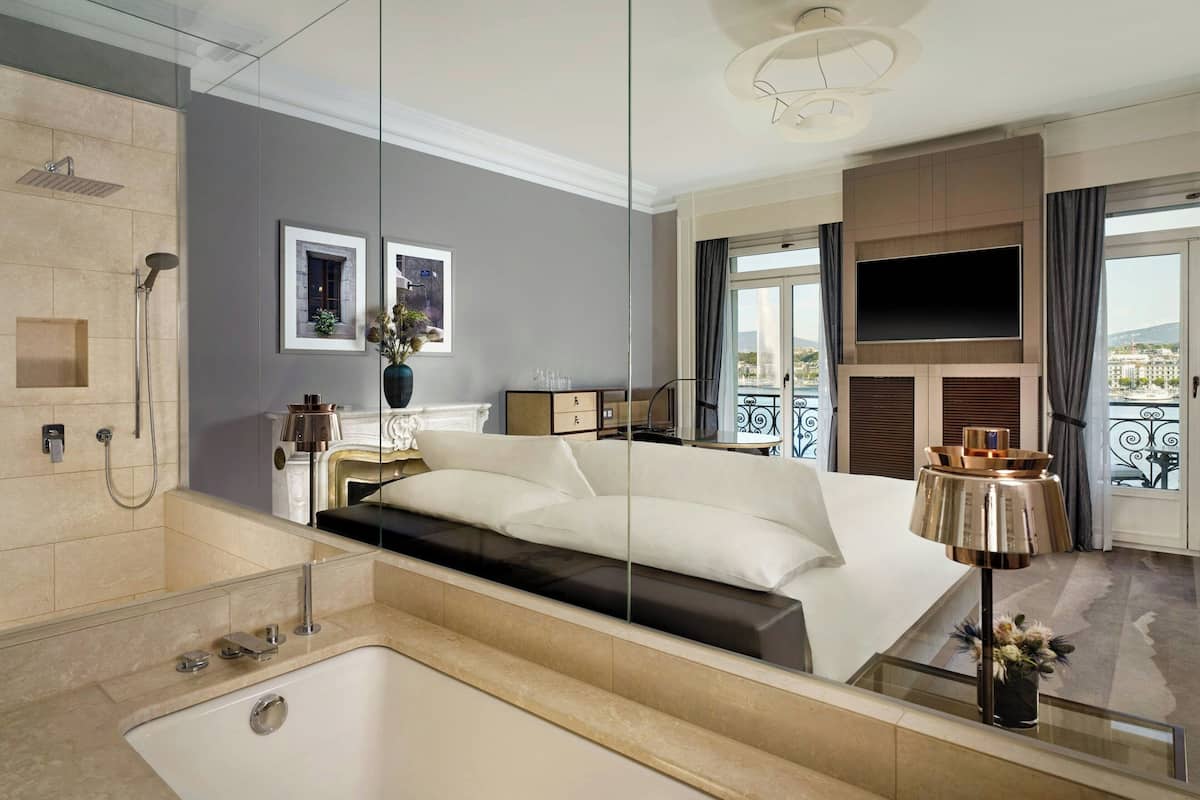 A modern hotel room with a large bed, a bathroom with a bathtub, a TV, and a balcony with a view.